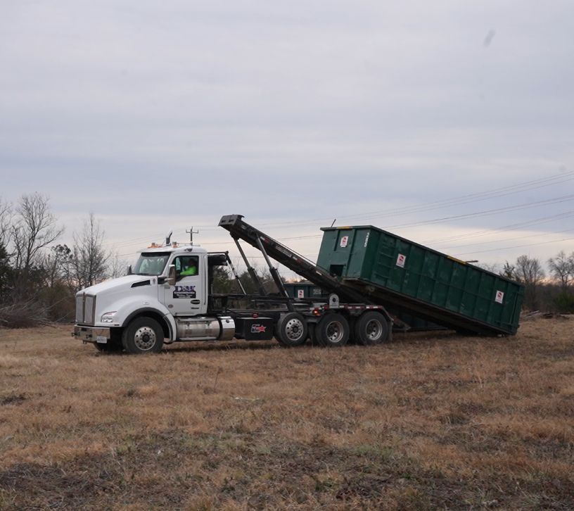 D&M roll off truck lifting a green dumpster into place