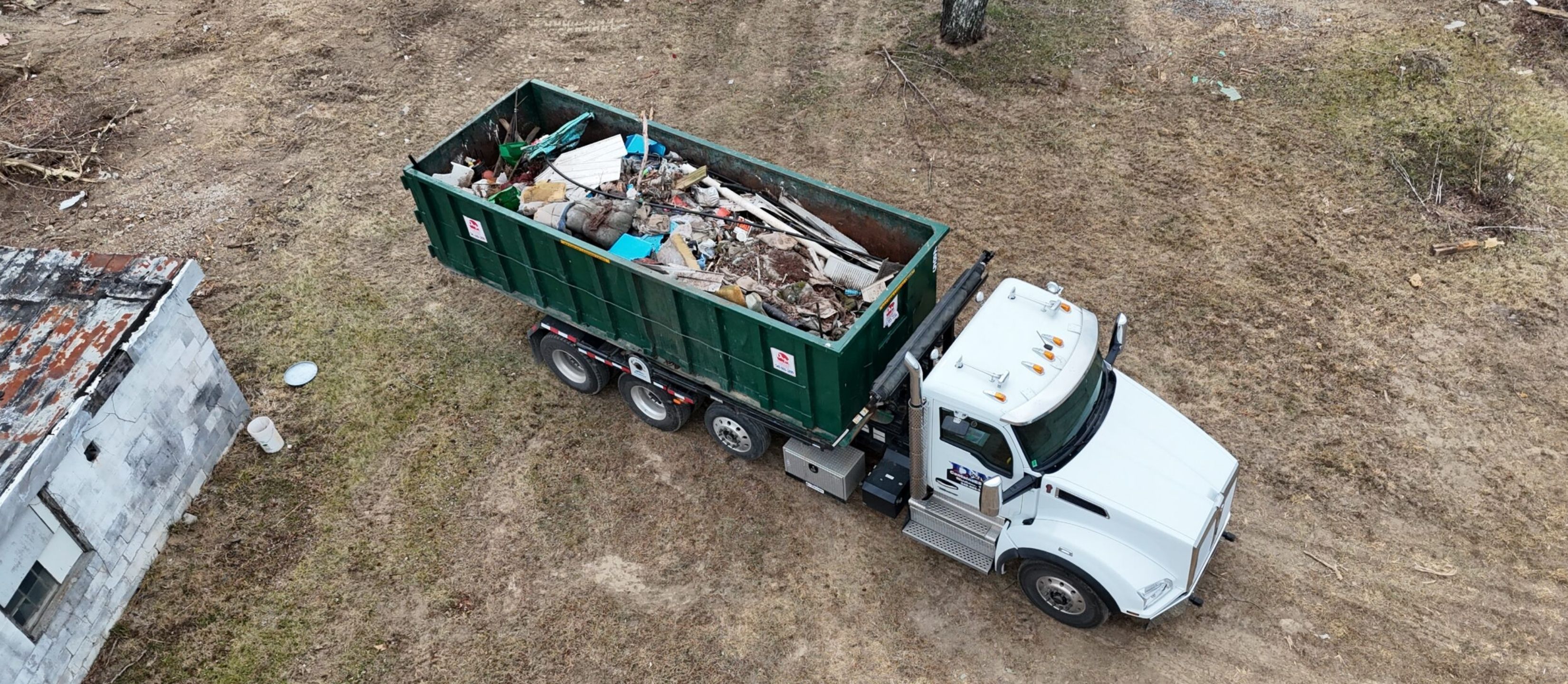 Drone view of a D&M Container Service roll off truck hauling a full green dumpster