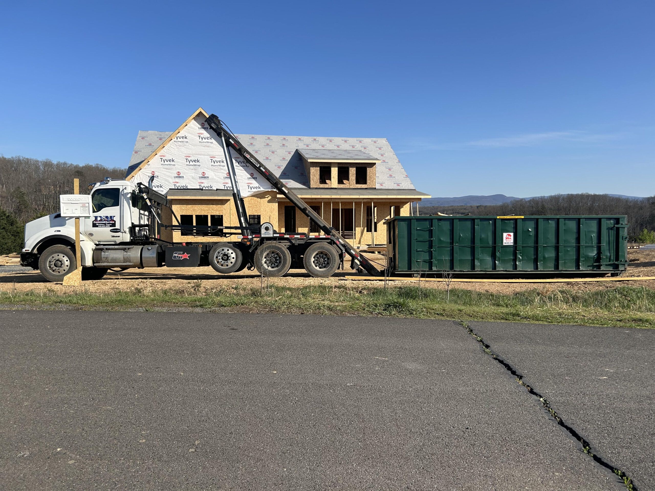 D&M Container Service roll off truck delivering a green dumpster to a new home build