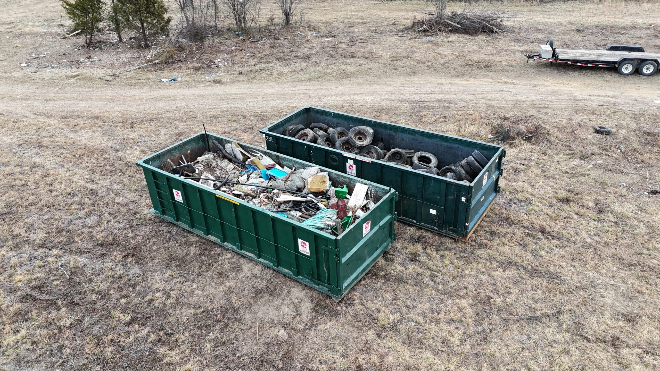 Two green D&M roll off dumpsters filled with debris and old tires, drone view