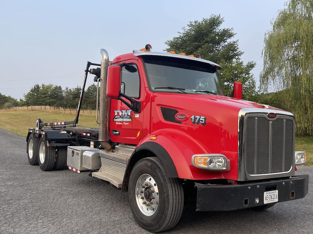 A red commercial tow truck with a black flatbed, white detailing, and chrome elements is parked on an asphalt road surrounded by grassy areas.